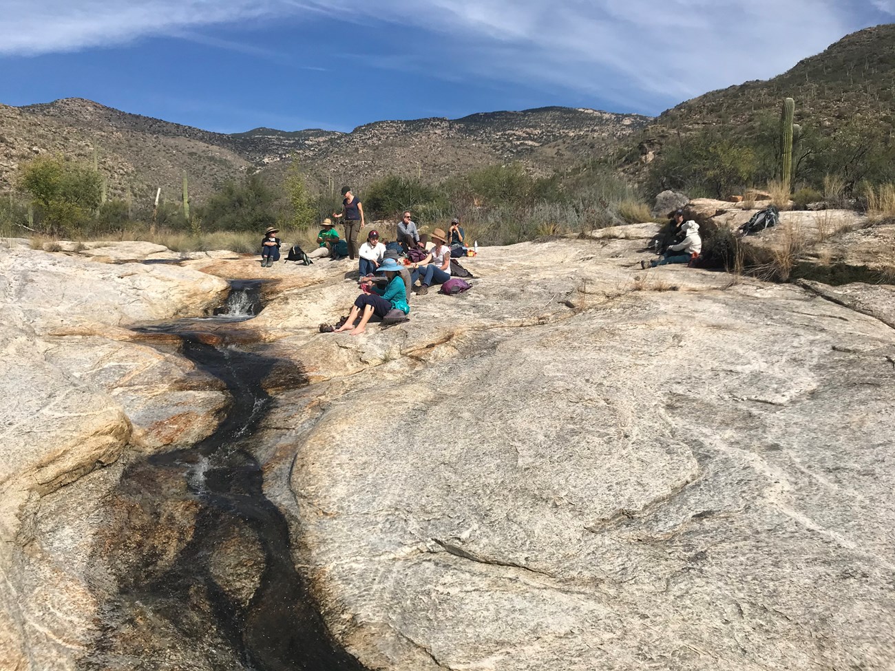 Volunteers resting on a bedrock. To their right is a stream of water flowing.