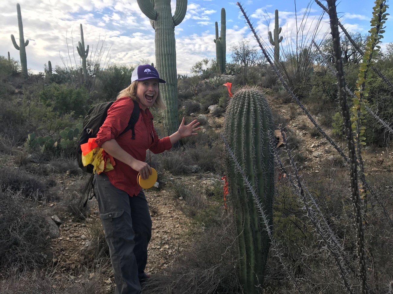 A woman posing next to a saguaro. She looks like she is about to high five it.