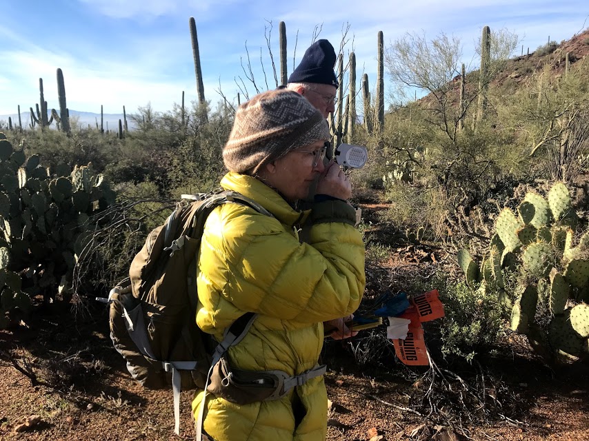 A woman wearing a yellow jacket looking through a clinometer