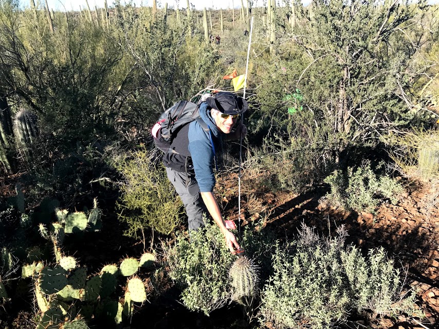 A person smiling. They are holding an unfolded white folding ruler while also holding a gps device.