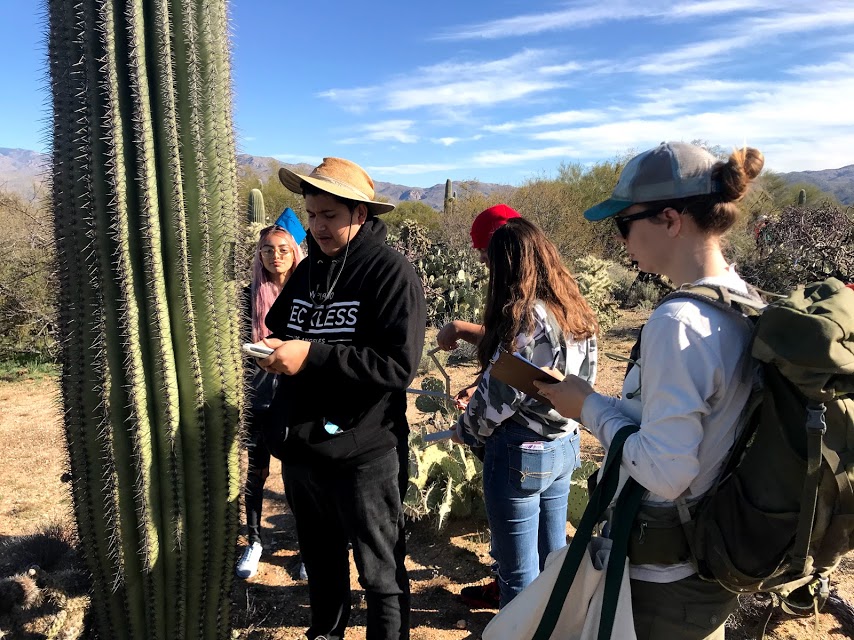 A student volunteer reading the coordinates from the GPS he is holding. A park staff is seen writing the data down on the data sheet.