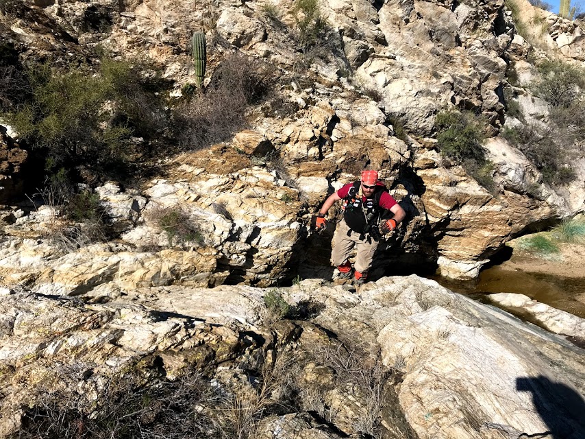 A man hiking up. Behind him is a body of water and a saguaro.