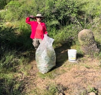 Volunteers flexes their bicep muscle and poses with a bag of invasive plants they have removed from the desert.