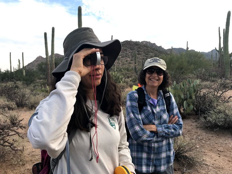 A woman smiling to the camera next to another woman using a clinometer