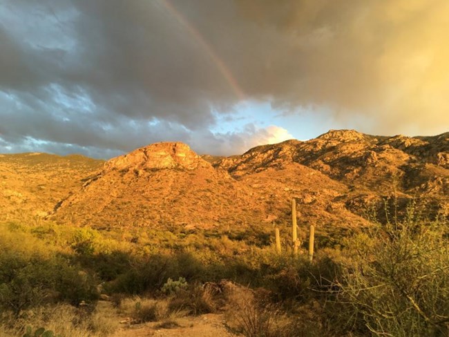 A rainbow appears over the sunlit mountain range