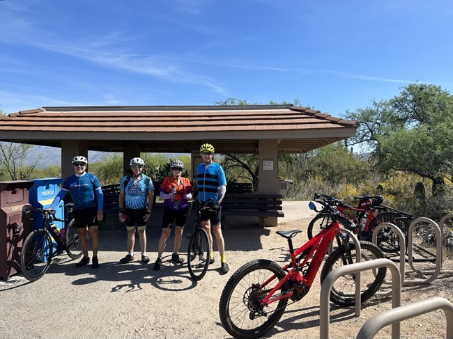 four cyclists stand in front of the bike ramada with their bikes