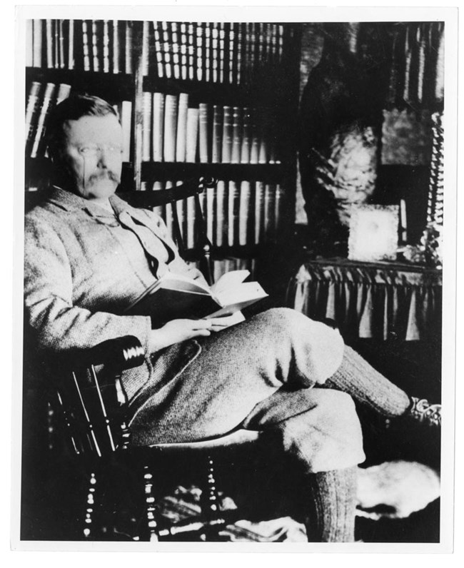 Theodore Roosevelt sitting in his Library with a book