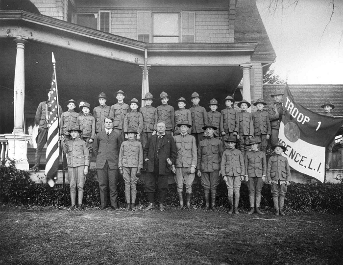A black and white photo of Theodore Roosevelt and several boy scouts posing on the porch of Sagamore Hill.