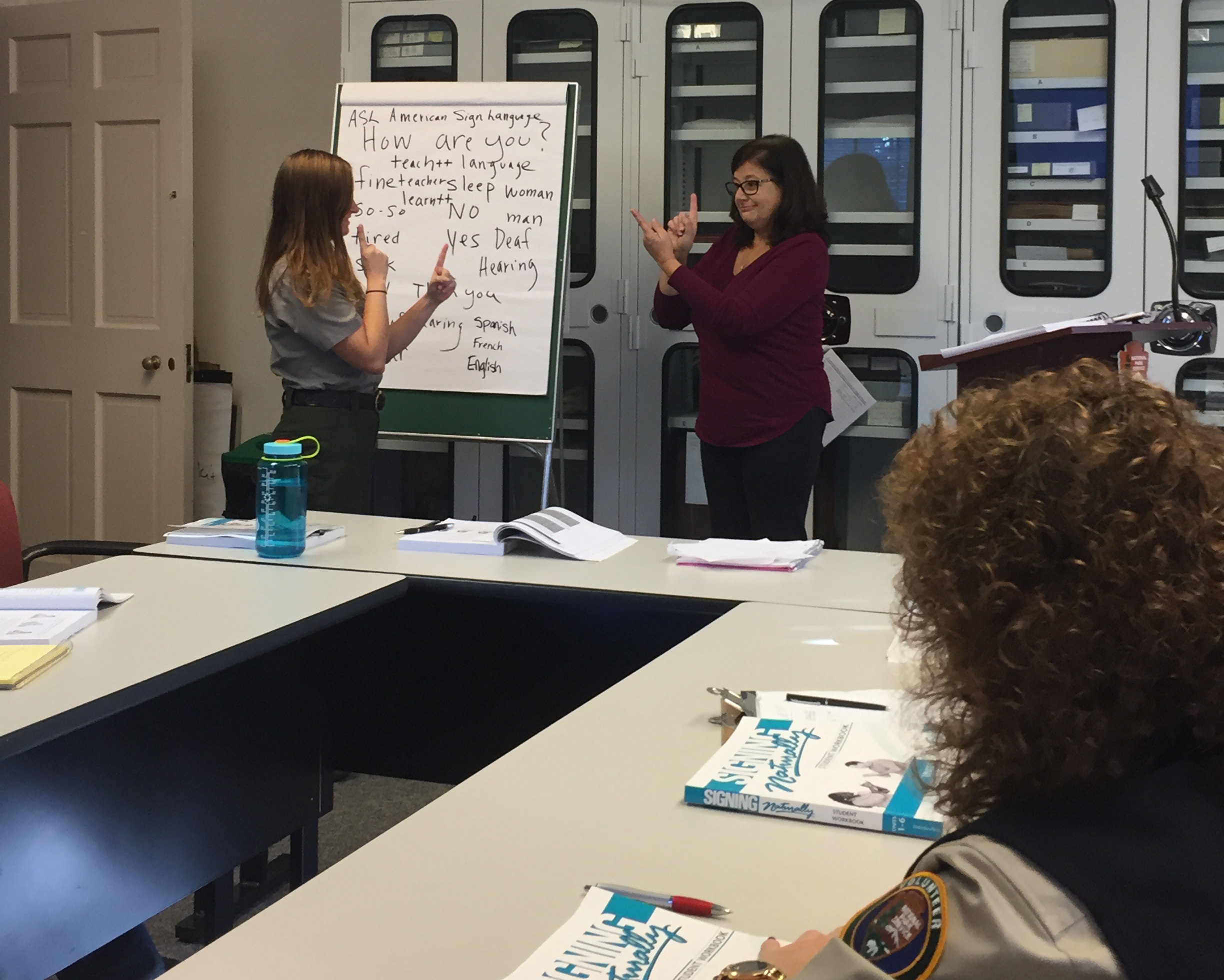 An instructor demonstrates signing for a park employee in a classroom setting.