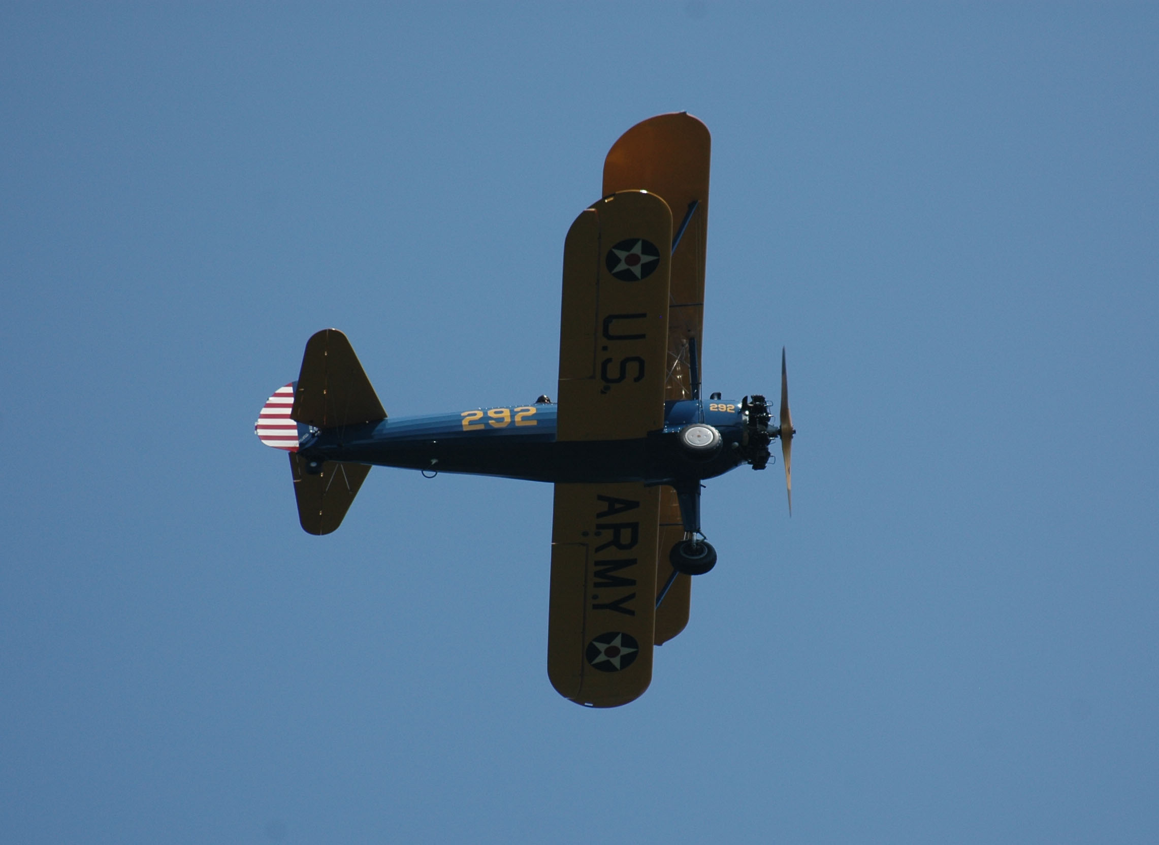 A yellow and blue historic biplane against blue sky.