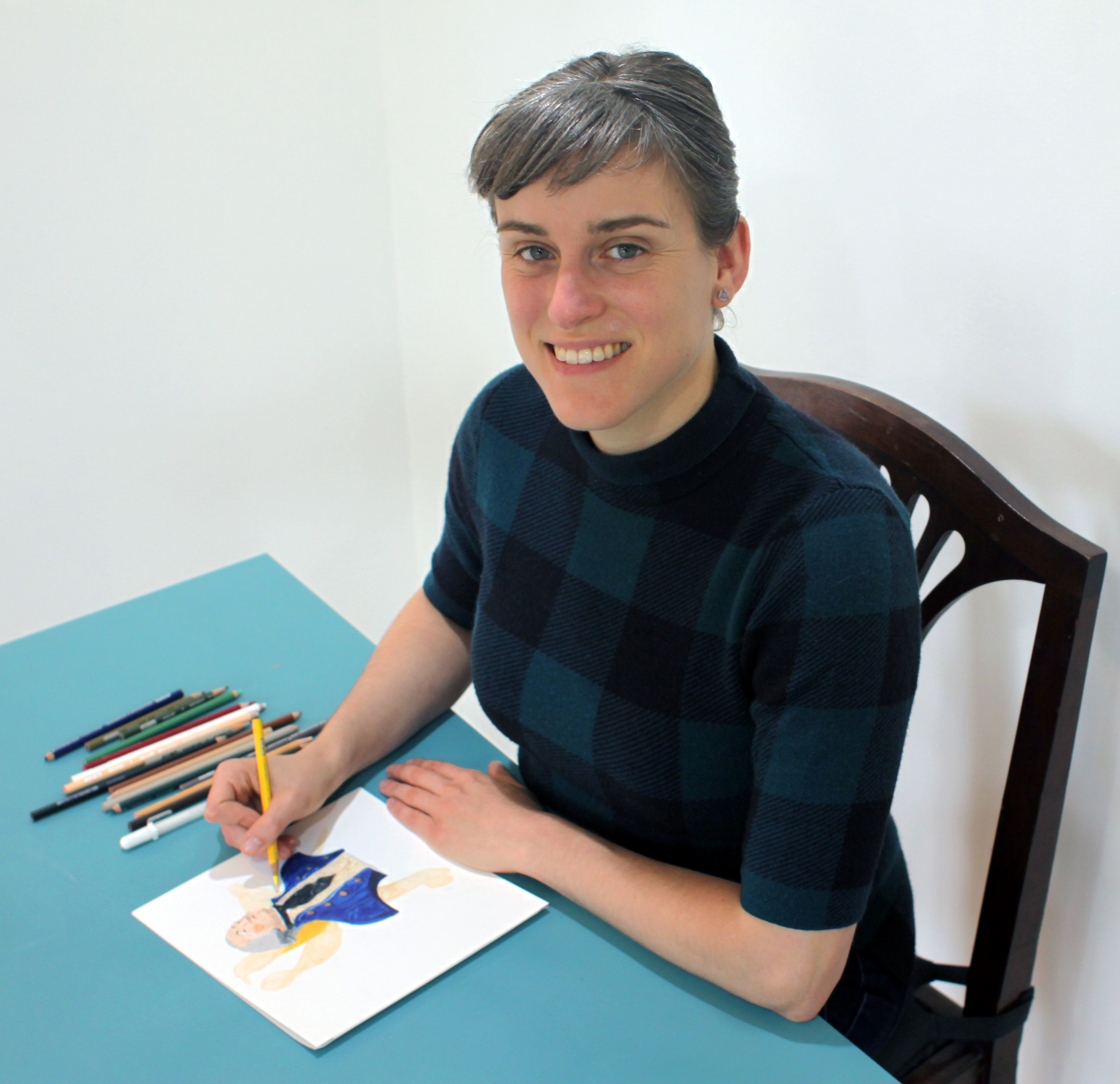 A smiling woman looks up from a color pencil drawing.