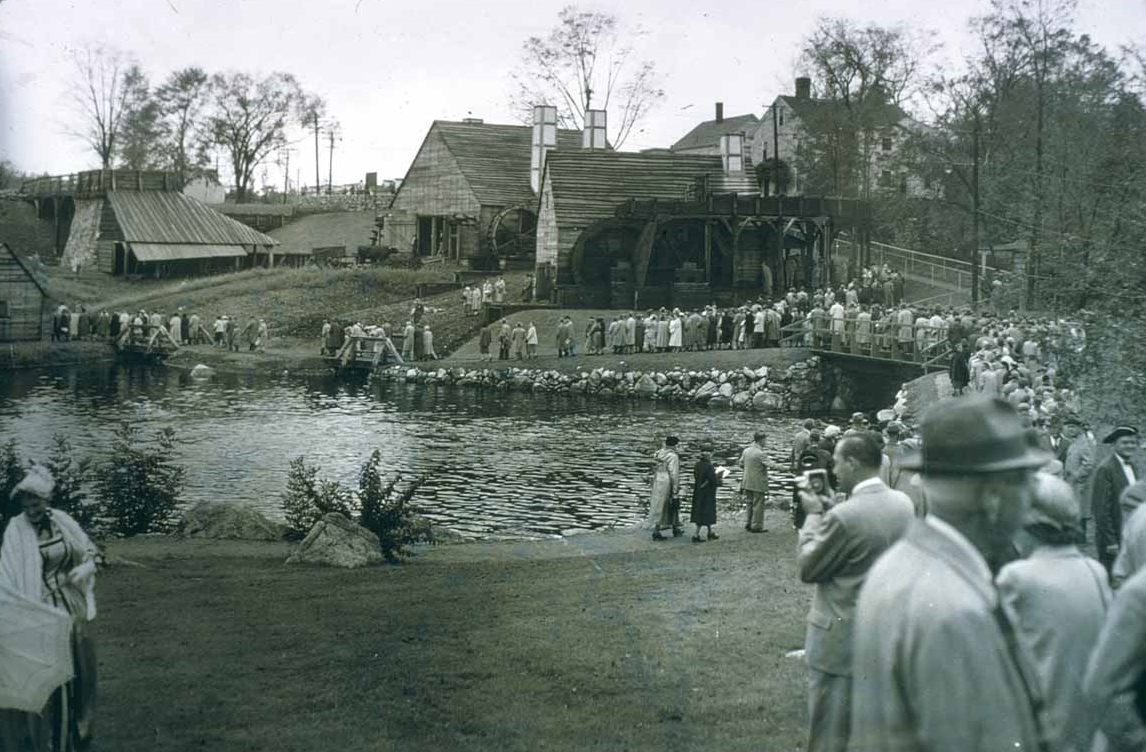 A black and white photograph of the iron works. The Saugus River is in the middle with the blast furnace, forge, and slitting mill on t he far side. Many people are crossing a bridge over the river and exploring the site. A black and white photograph of the iron works. The Saugus River is in the middle with the blast furnace, forge, and slitting mill on t he far side. Many people are crossing a bridge over the river and exploring the site.