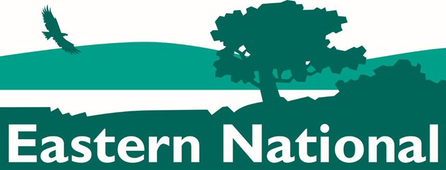 Silhouette of a bird flying over a field of trees with Eastern National at bottom