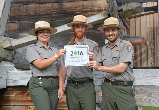 Saugus Iron Works Park Rangers Hold Up a Sign with the 2016 Centennial Logo