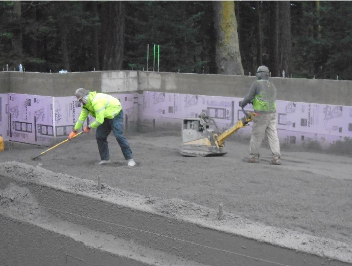 Conveyor belt distributing gravel overhead while construction works work below on distributing and compacting the gravel evenly.