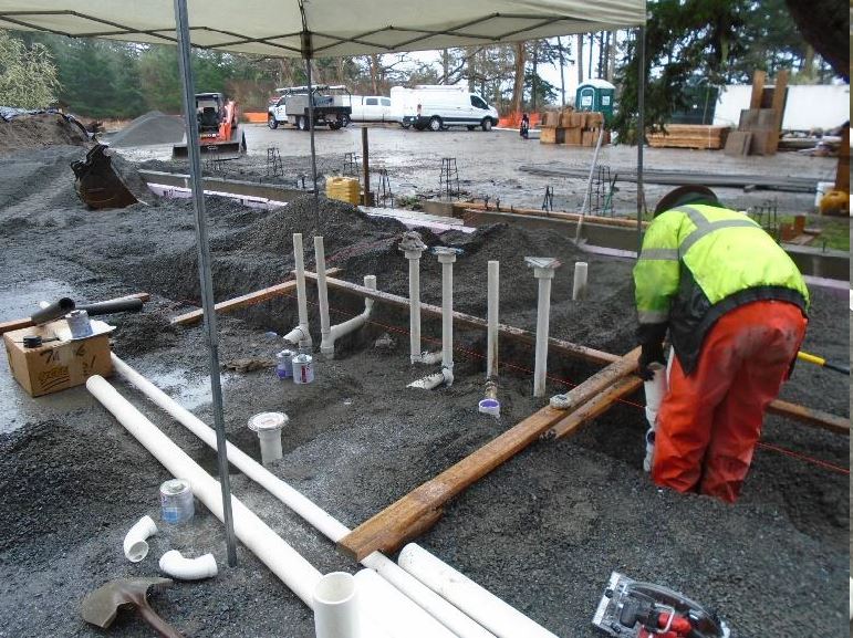 A construction worker works under a tent out of the rain to install PVC pipes for waste lines and electrical conduit