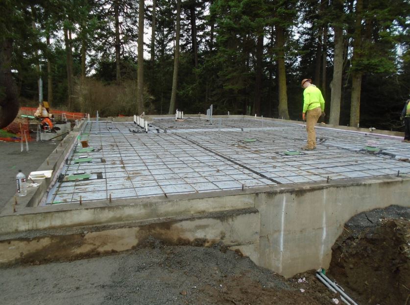 A construction worker stands in the middle of the building foundation among rebar grid pattern which is ready for a cement pour for the foundation slab.