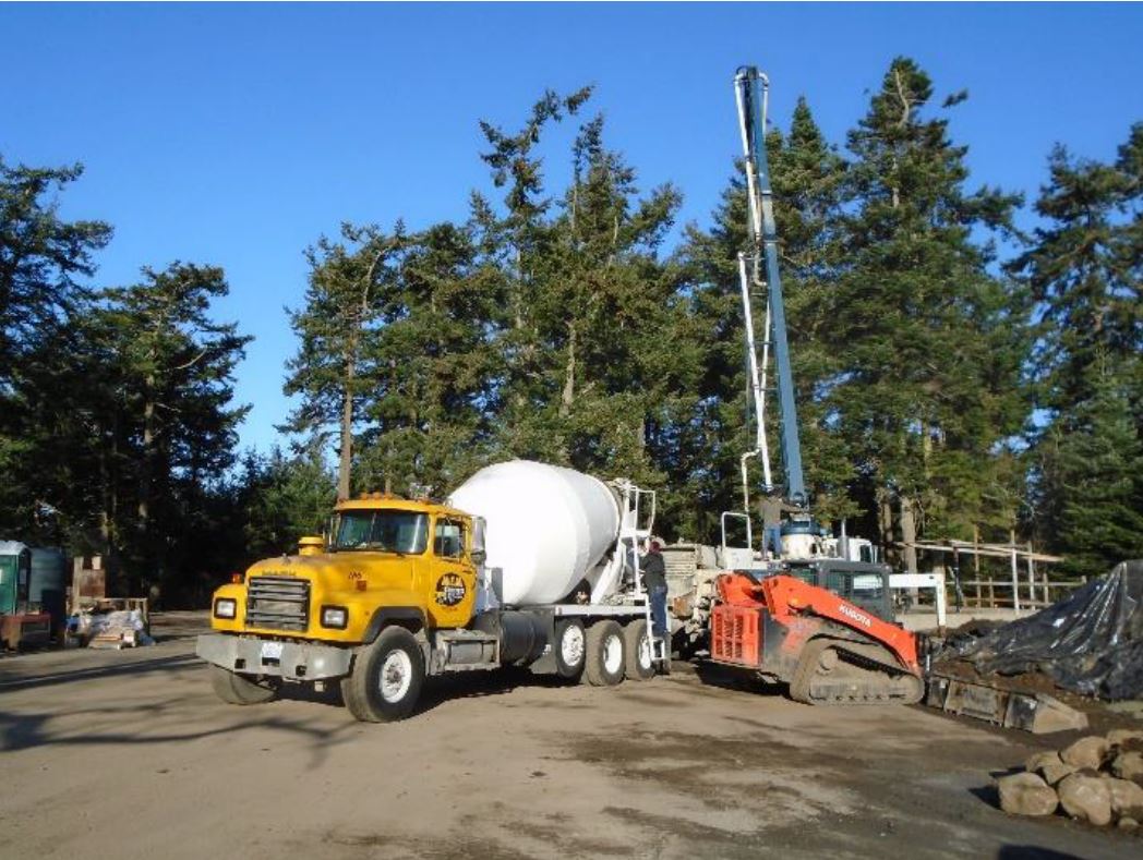 A concrete truck with a crane is staged in the foreground while concrete operations happen in the background