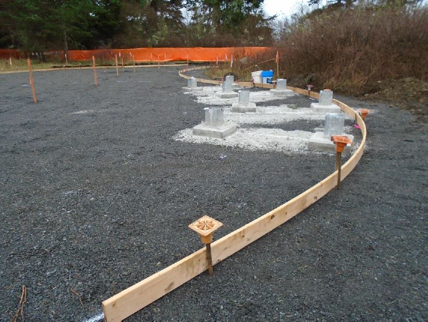A thin wooden board wraps along anchored rebar on a graveled area to create a frame for a future cement pour
