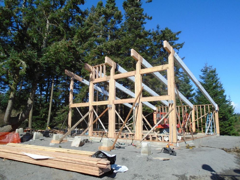A wooden building frame with a shed roof style is framed with stress-rated engineer wood beams for the exterior walls and roof, while horizonal wood beams frame out window placement