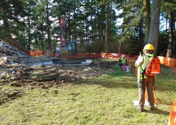 A National Park Service archeologist stands in the foreground monitoring the excavation of the old visitor center slab foundation