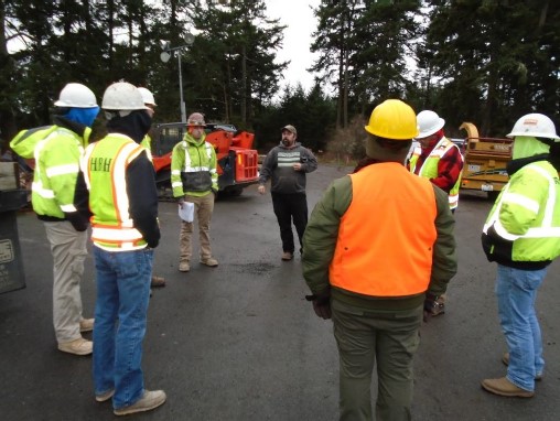 A group of contractors and park staff stand in a circle and talk about archeological and historic significance of the site prior to construction work