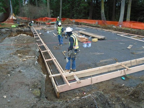 Four construction workers build a wooden frame for the building’s cement footing on the prepped sub-layer site