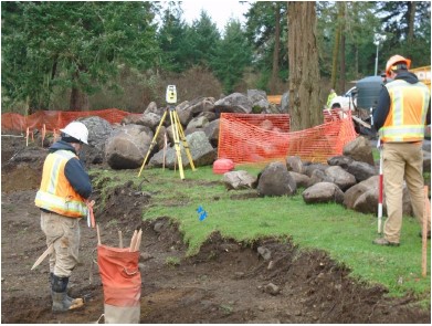 Surveyors in construction safety vests and hard hats use survey equipment to find the edges of a construction area