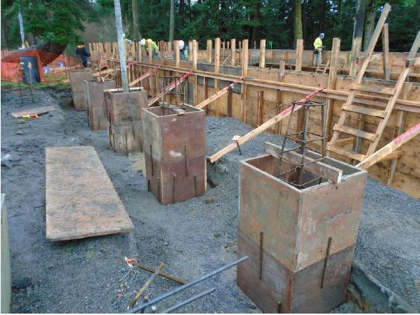 Five square boxes made of wooden panels and reinforcing steel are being installed at the entry of the building foundation