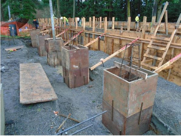 Five square boxes made of wooden panels and reinforcing steel are being installed at the entry of the building foundation