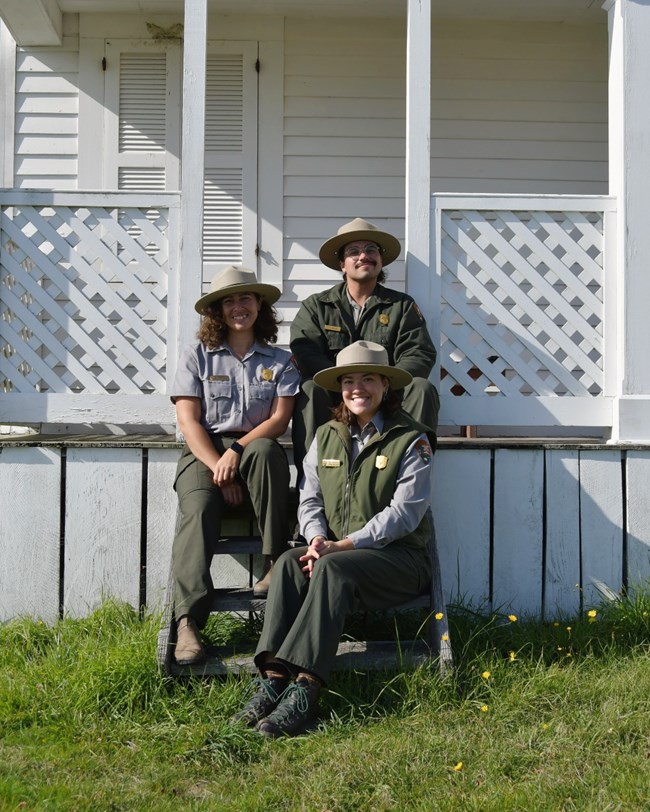 Three park rangers sit on the steps of a white historic building