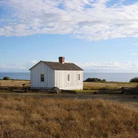 Color photograph of a whitewashed building on a prairies with blue cloudy skies behind it.