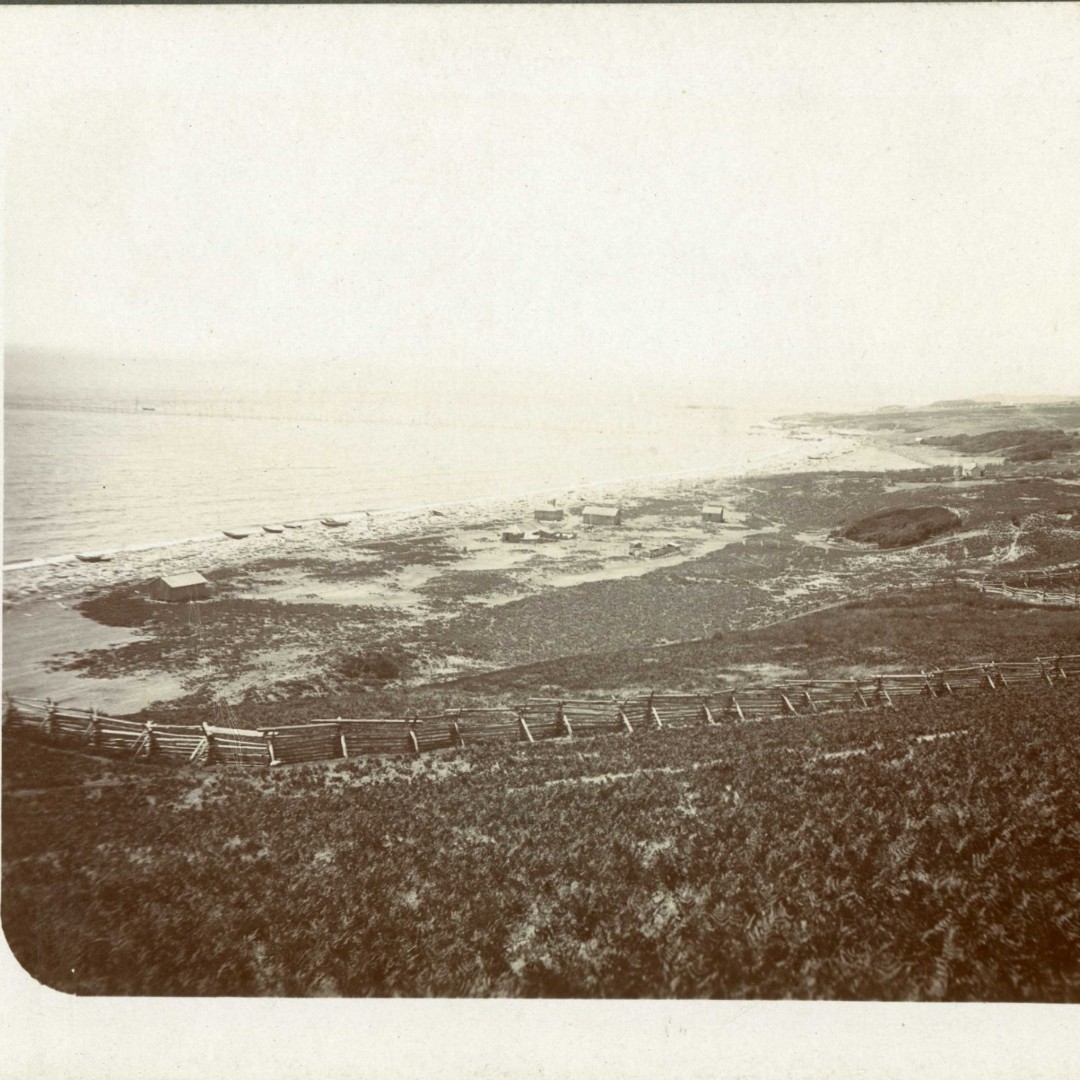 Fishermen's cabins along South Beach, post-military period, late 19th century or turn of the century. Background shows fish weir extending out into the Strait of San Juan de Fuca. Various canoe types on the shore.