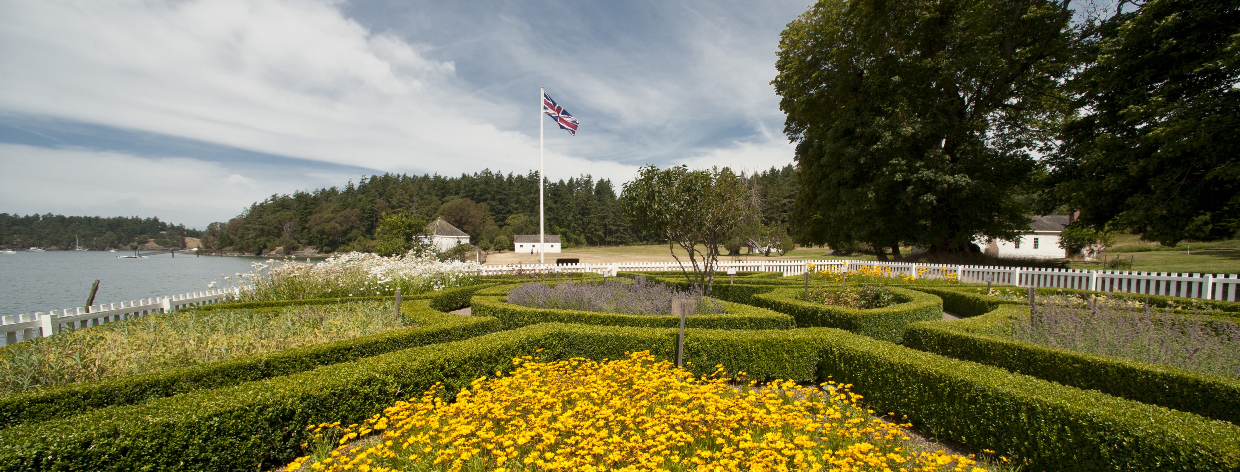 A flower garden with hedges and historic white buildings behind