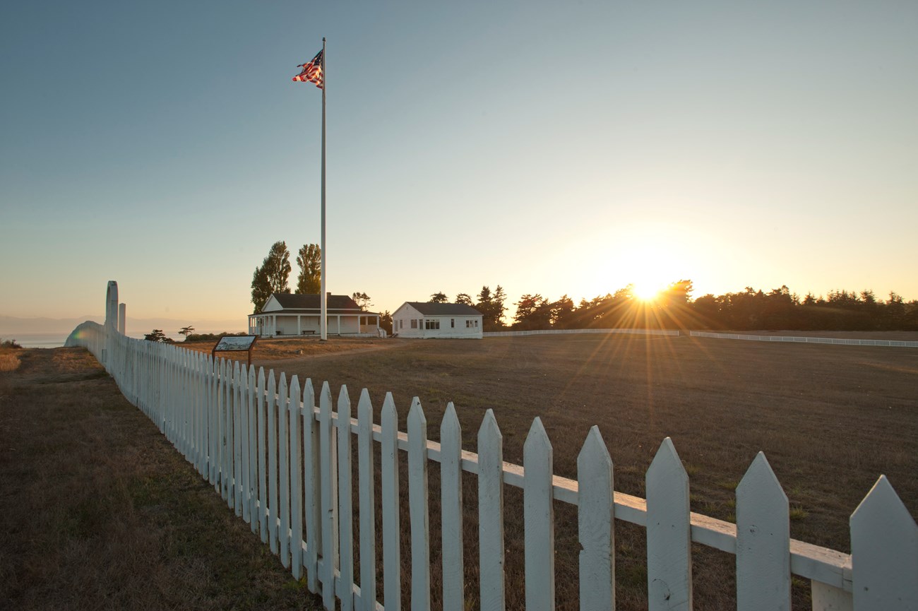 The sun setting behind a white pickett fence.