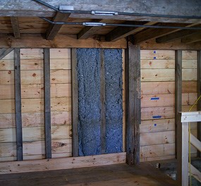 Bright blue insulation batts are mounted between studs on the second floor of the store house.