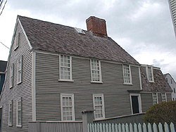 The Narbonne House is a two story grey house. On the left of the center chimney is a peaked roof, and on the right is a lower barn like, or gambrel roof. The Narbonne House is a two story grey house. On the left of the center chimney is a peaked roof, and on the right is a lower barn like, or gambrel roof.