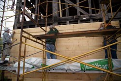 workmen on a scaffold attach sheathing to the frame of the building.