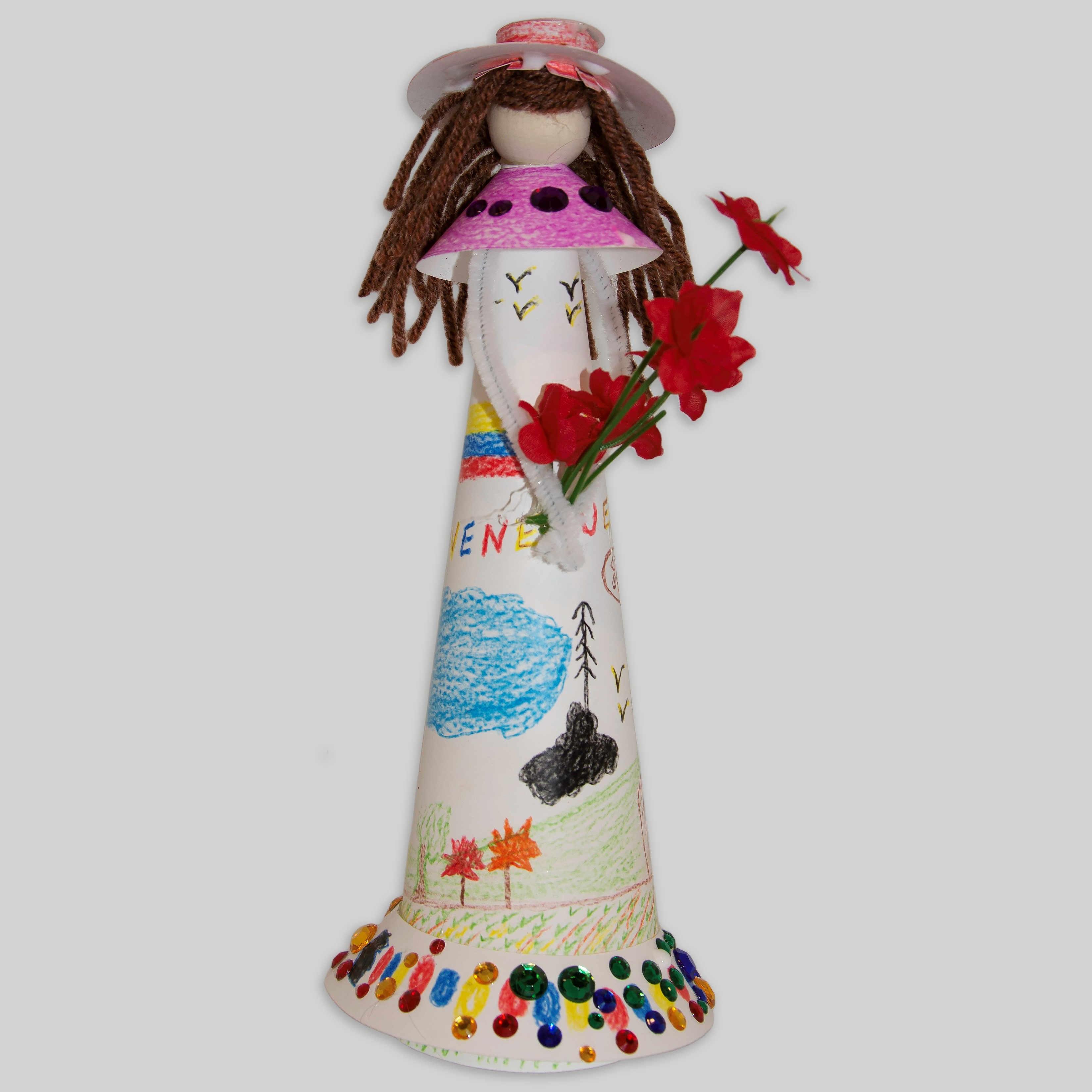 A paper faceless doll with long brown hair, colorful hat and dress, holding red flowers.
