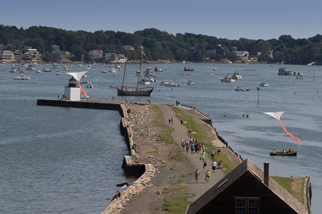 Festival goers walk along wharf as boats motor past and kites fly above
