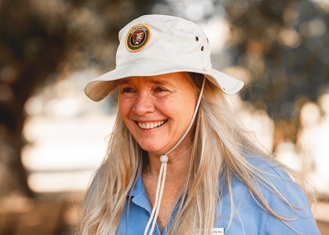 Woman in volunteer hat smiling of the the side of the camera.
