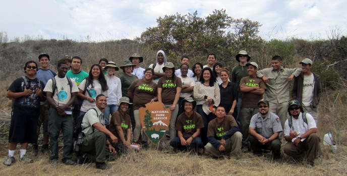 A group of young volunteers pose with a large National Park Service arrowhead