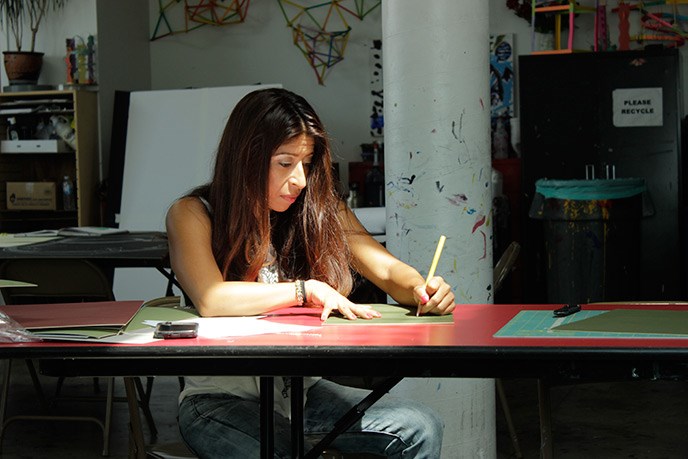 A young woman works on an art project in a studio, her face illuminated by natural light A young woman works on an art project in a studio, her face illuminated by natural light