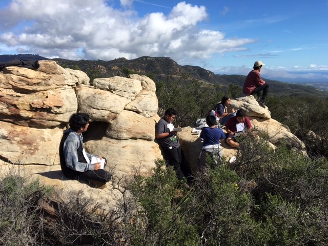 Youth seated outdoors on rocks while writing and sketching Youth seated outdoors on rocks while writing and sketching