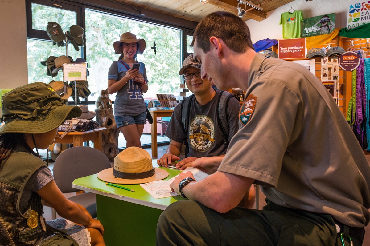Ranger in uniform smiling swearing in Junior Rangers around a table with a flat hat on it.