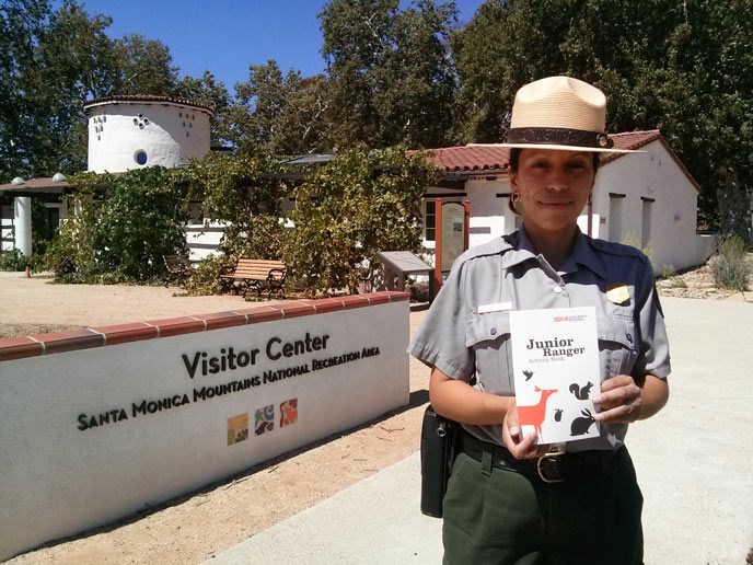 A park ranger holds a small activity book and poses in front of the visitor center A park ranger holds a small activity book and poses in front of the visitor center