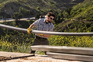 Ranger in uniform holding a large metal rail with mountains in the background.