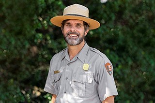 Man standing in a park service uniform smiling at the camera.