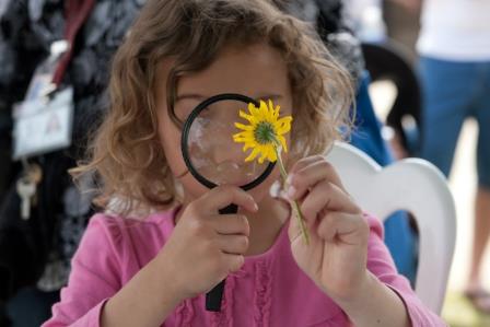 Girl inspects flower with magnifying glass.