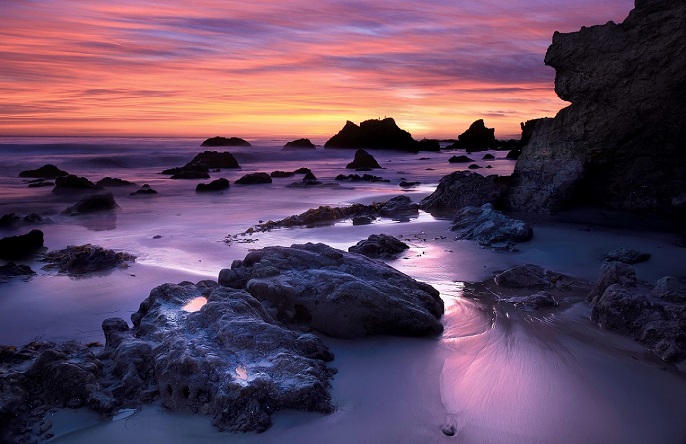 Beach shore rocks and a warm looking sunset in the background